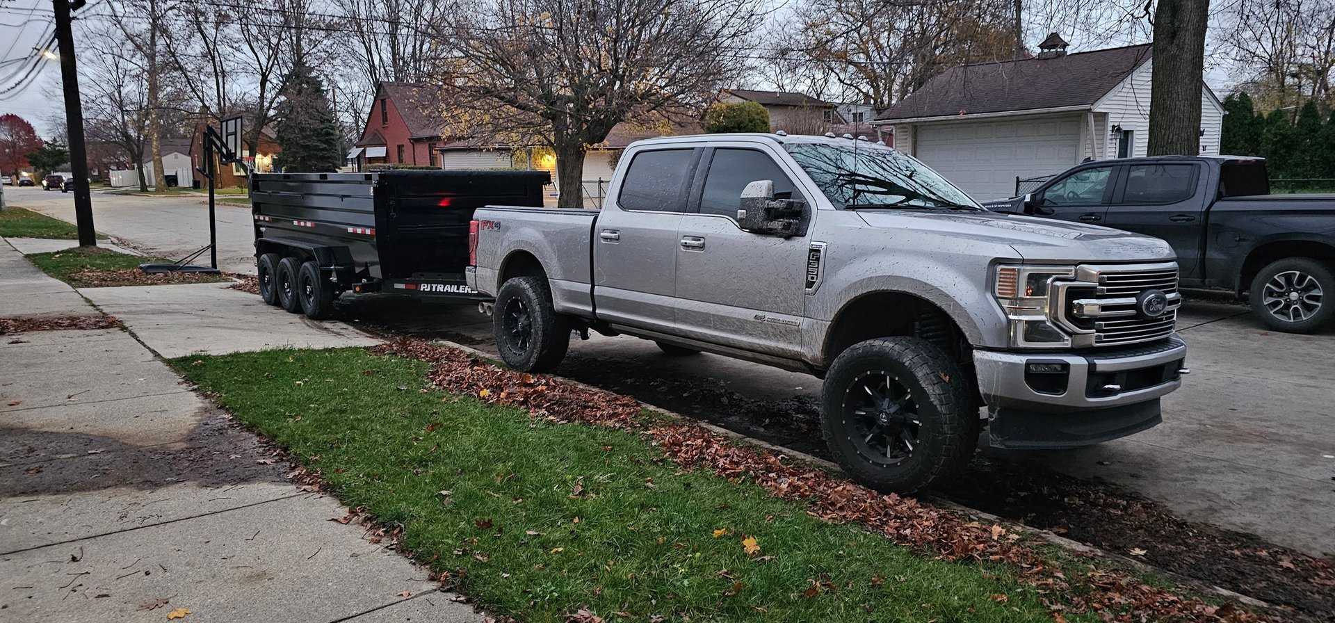 Silver Ford F-250 Super Duty pickup truck parked on a residential street with a utility trailer and homes in the background